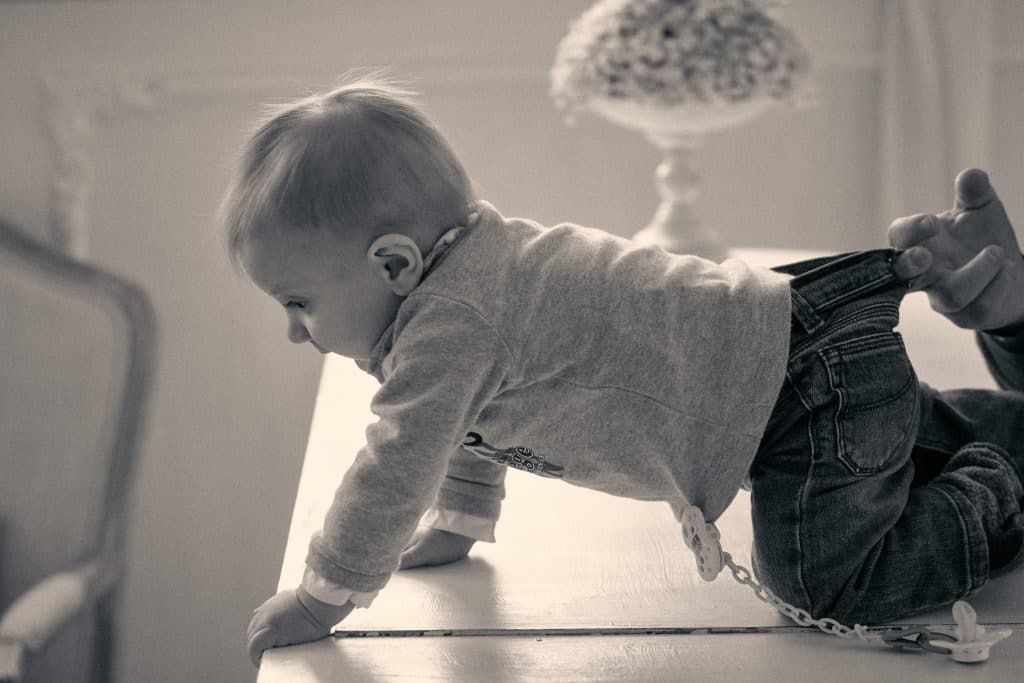Baby in white outfit crawling on floor next to black handbag in soft lighting - © Pascal Recchia. All rights reserved.