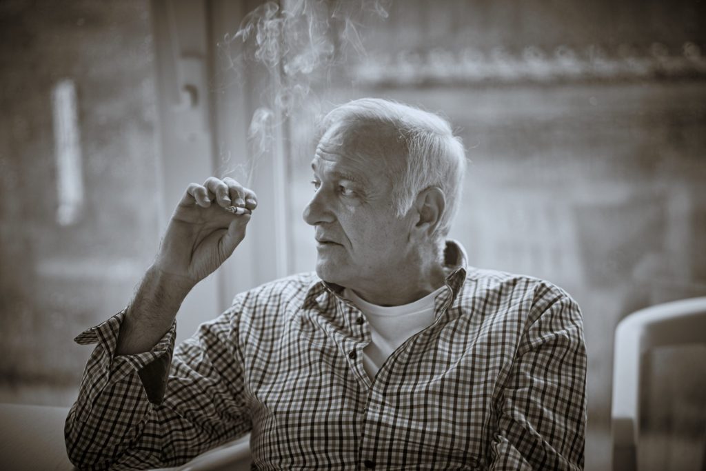 Elderly man in checkered shirt smoking cigarette indoors, black and white vintage style photograph - © Pascal Recchia. All rights reserved.