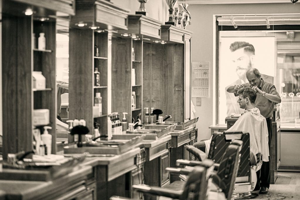 Classic barbershop interior with vintage chairs, mirrors, and barber cutting client's hair in black and white photo - © Pascal Recchia. All rights reserved.