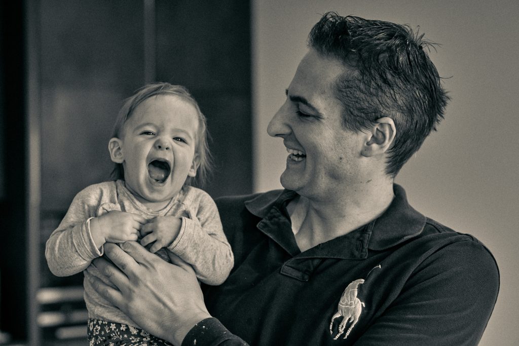 Father and young child laughing together indoors, both with mouths open in joyful expression, black and white photo - © Pascal Recchia. All rights reserved.