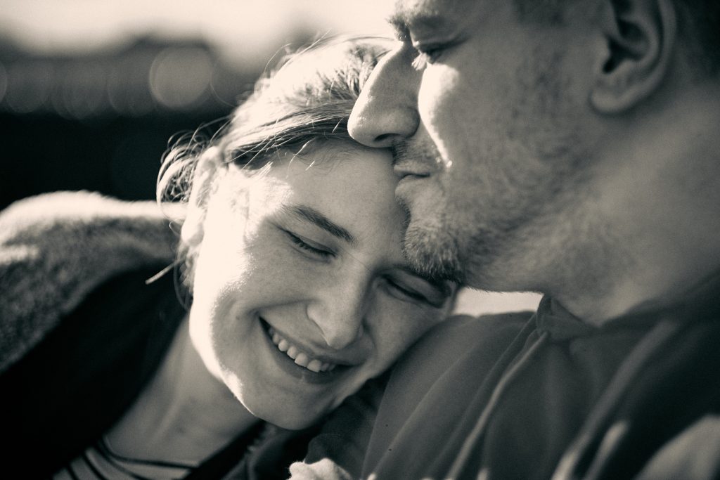 Black and white intimate portrait of smiling couple embracing, woman laughing with eyes closed, man close to her forehead
