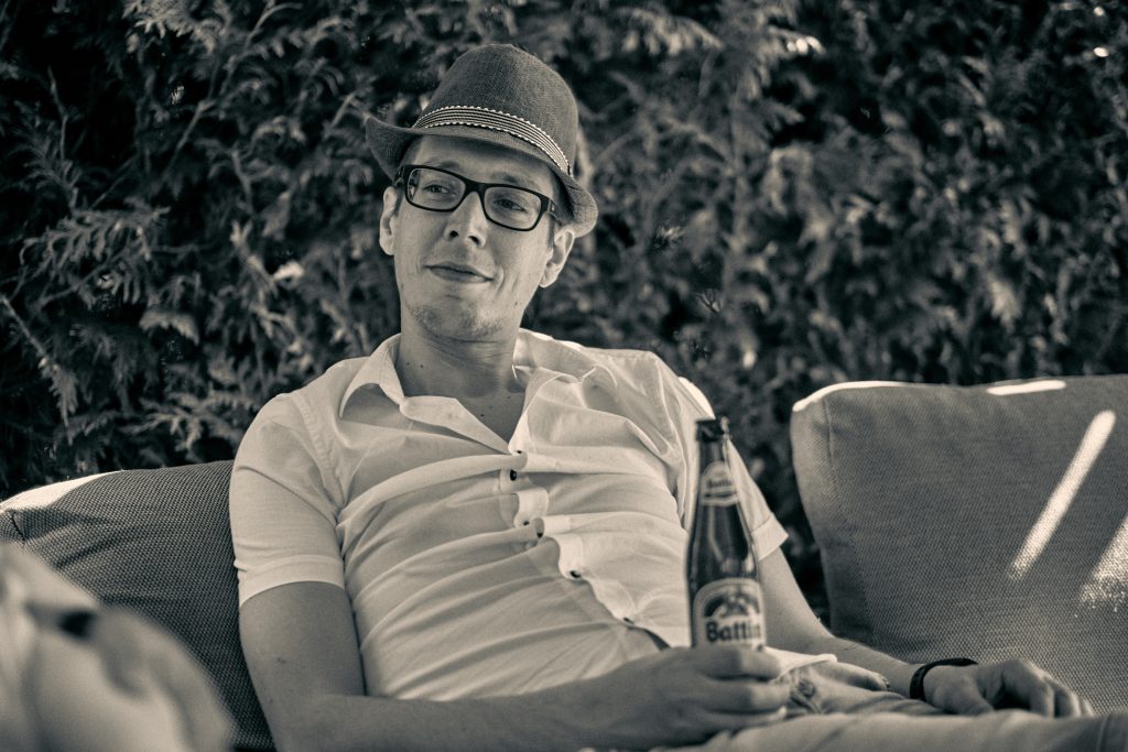 Man in fedora hat and glasses sitting relaxed on outdoor furniture with beer bottle in hand, vintage sepia-toned photo - © Pascal Recchia. All rights reserved.