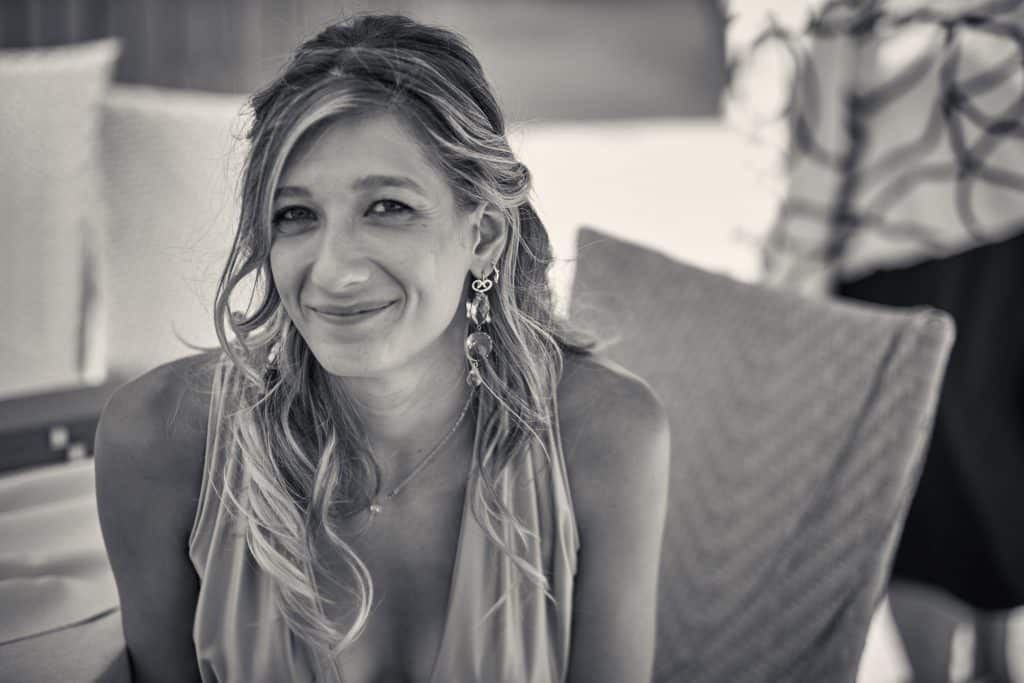 Smiling woman with long wavy blonde hair and dangling earrings sitting on chair in warm sepia-toned portrait photograph - © Pascal Recchia. All rights reserved.