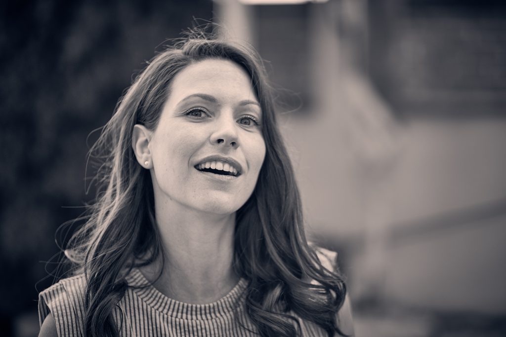 Smiling woman with long dark hair wearing striped sweater looking up joyfully in warm sepia-toned portrait photograph - © Pascal Recchia. All rights reserved.