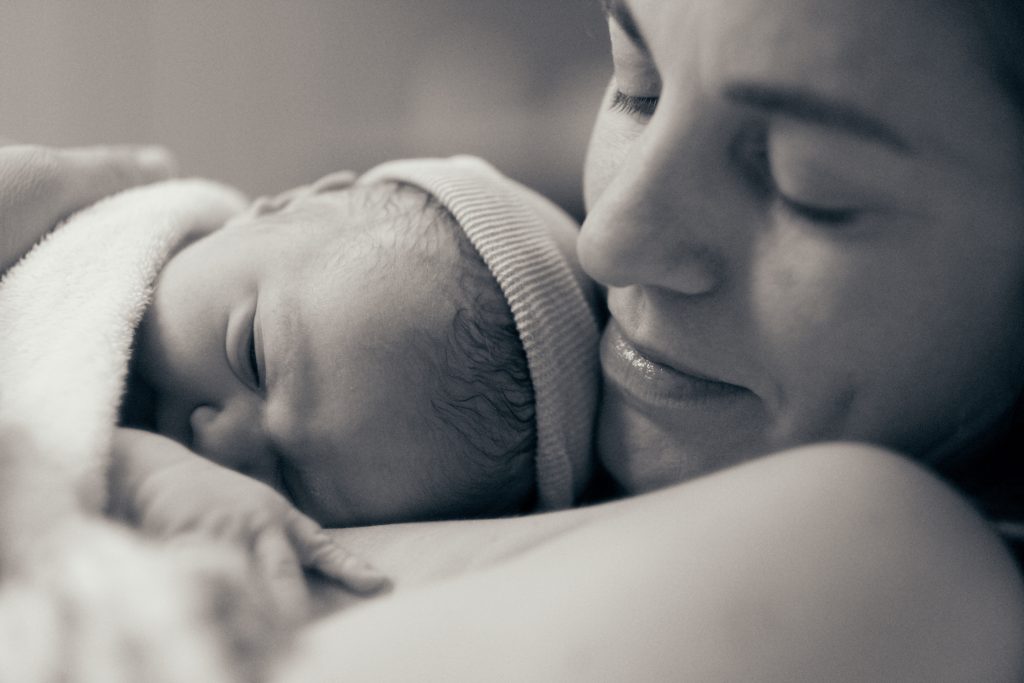 Newborn baby with knit hat sleeping peacefully in mother's loving embrace, black and white intimate family portrait - © Pascal Recchia. All rights reserved.