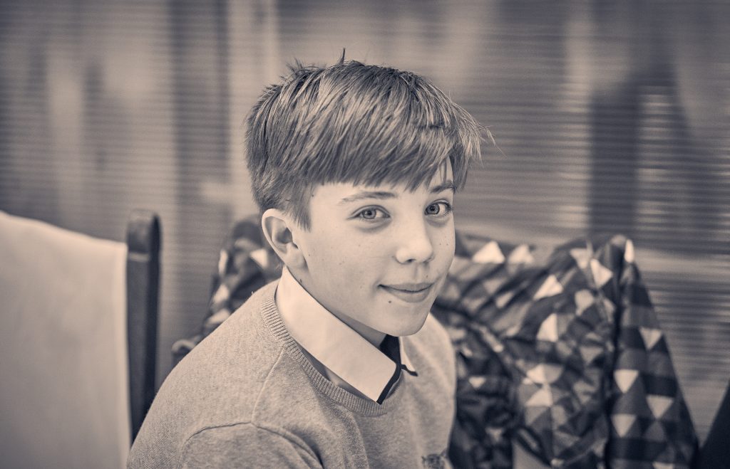 Young person with short layered hair and shirt smiling at camera in sepia-toned portrait with blurred background - © Pascal Recchia. All rights reserved.