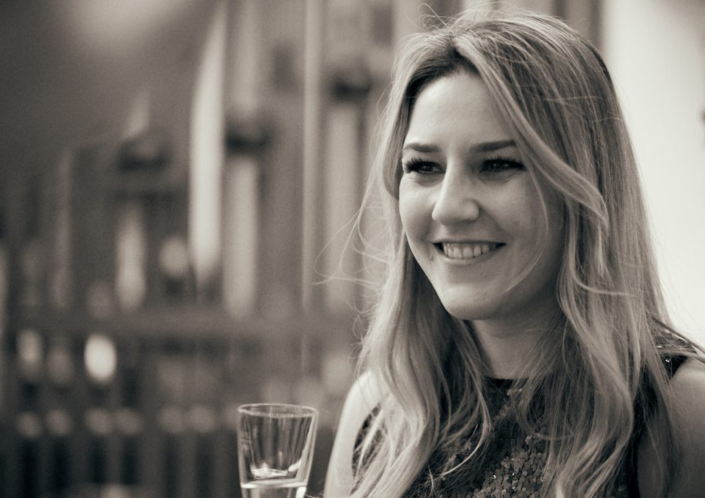 Smiling blonde woman holding glass in sepia-toned portrait photo with blurred background - © Pascal Recchia. All rights reserved.