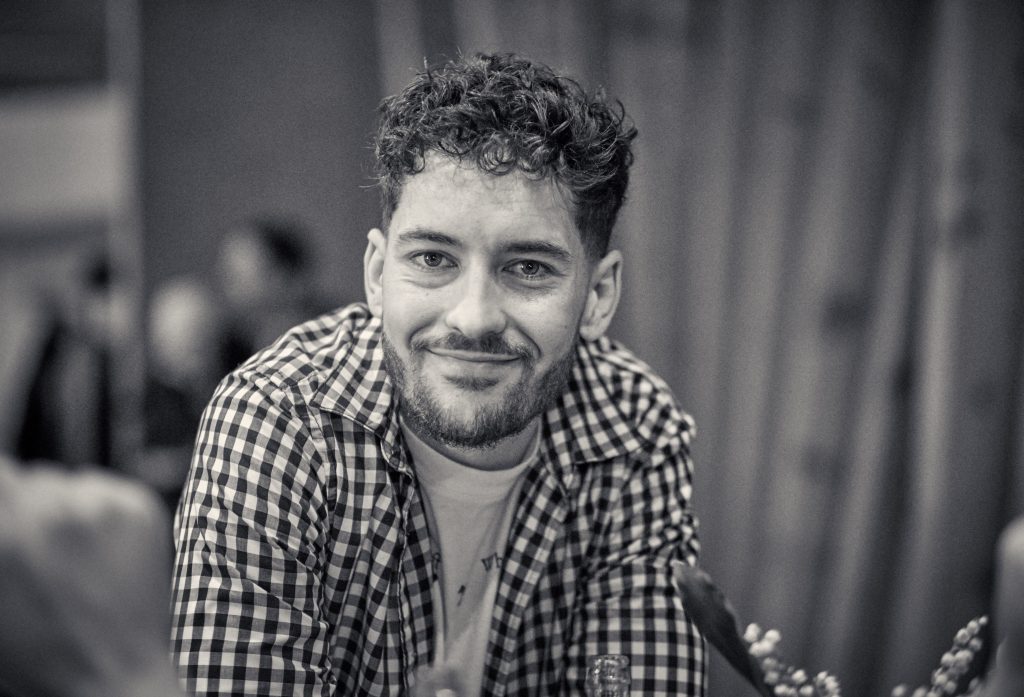 Young man with curly hair smiling warmly at camera, wearing checkered shirt in black and white portrait photo - © Pascal Recchia. All rights reserved.