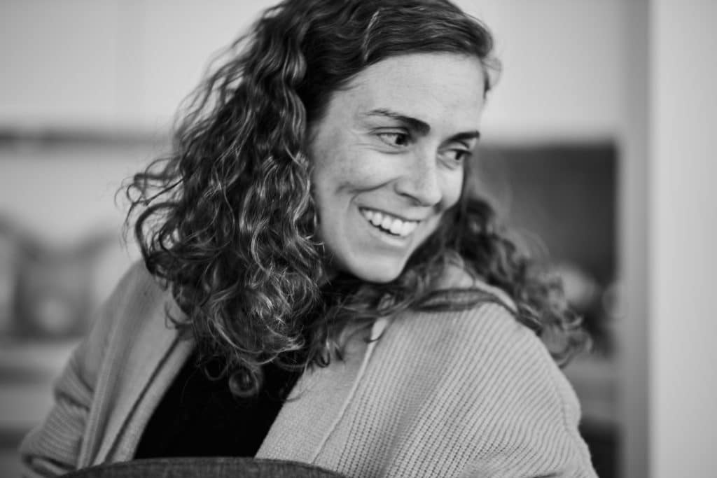 miling woman with curly dark hair wearing a ribbed sweater, captured in warm sepia-toned black and white photography - © Pascal Recchia. All rights reserved.