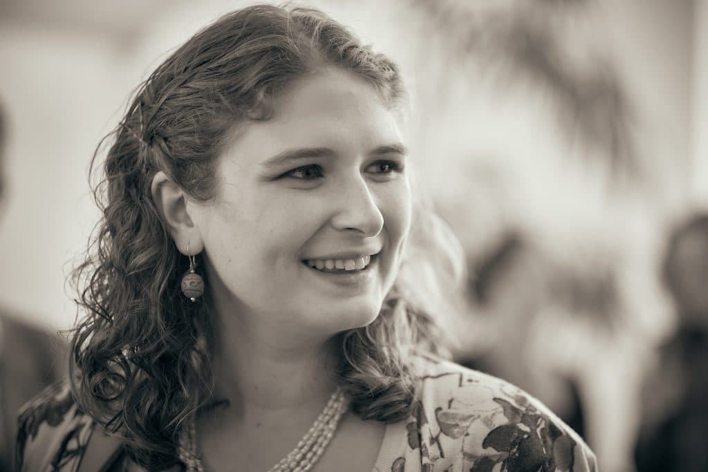 Young woman with curly hair and earrings smiling warmly in sepia-toned portrait with soft background blur - © Pascal Recchia. All rights reserved.