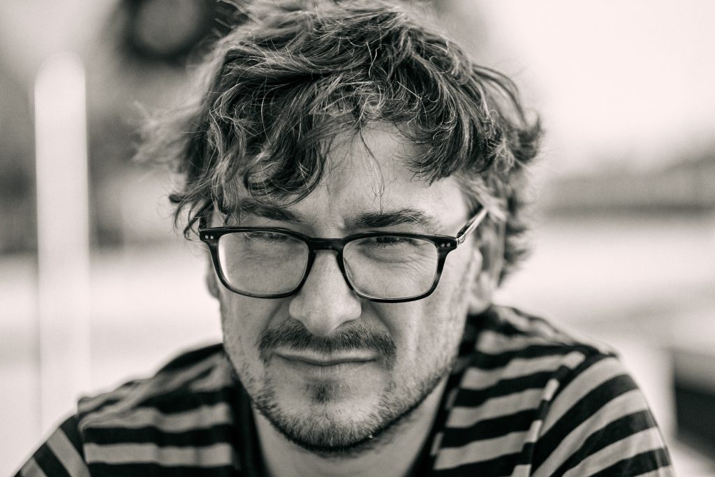 Black and white portrait of man with glasses, curly hair, and mustache and beard wearing striped shirt - © Pascal Recchia. All rights reserved.
