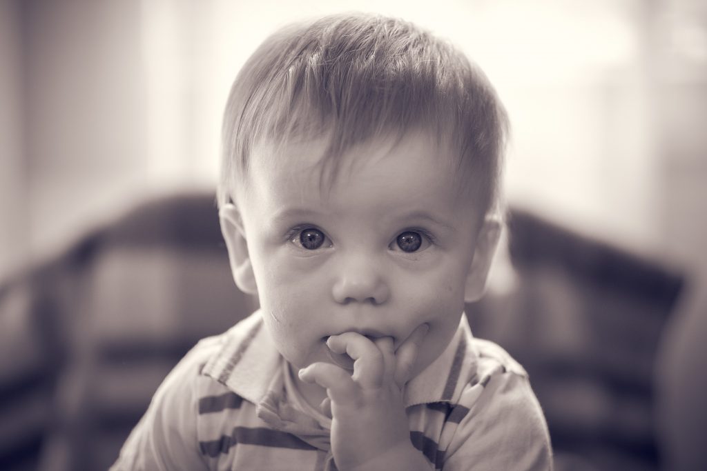 Young toddler with blonde hair in striped shirt looking thoughtfully at camera with finger in the mouth in sepia-toned photo - © Pascal Recchia. All rights reserved.