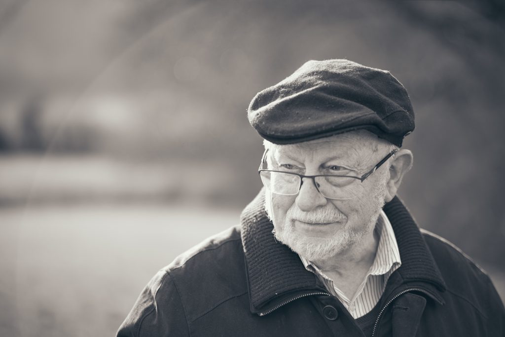 Elderly man with glasses wearing flat cap and dark jacket, smiling warmly in sepia-toned portrait photograph - © Pascal Recchia. All rights reserved.