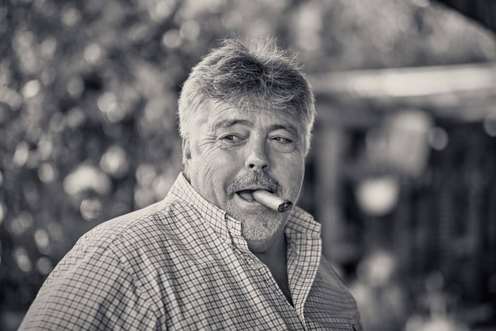 Black and white portrait of middle-aged man with gray hair and mustache smoking cigar, wearing checkered shirt outdoors - © Pascal Recchia. All rights reserved.