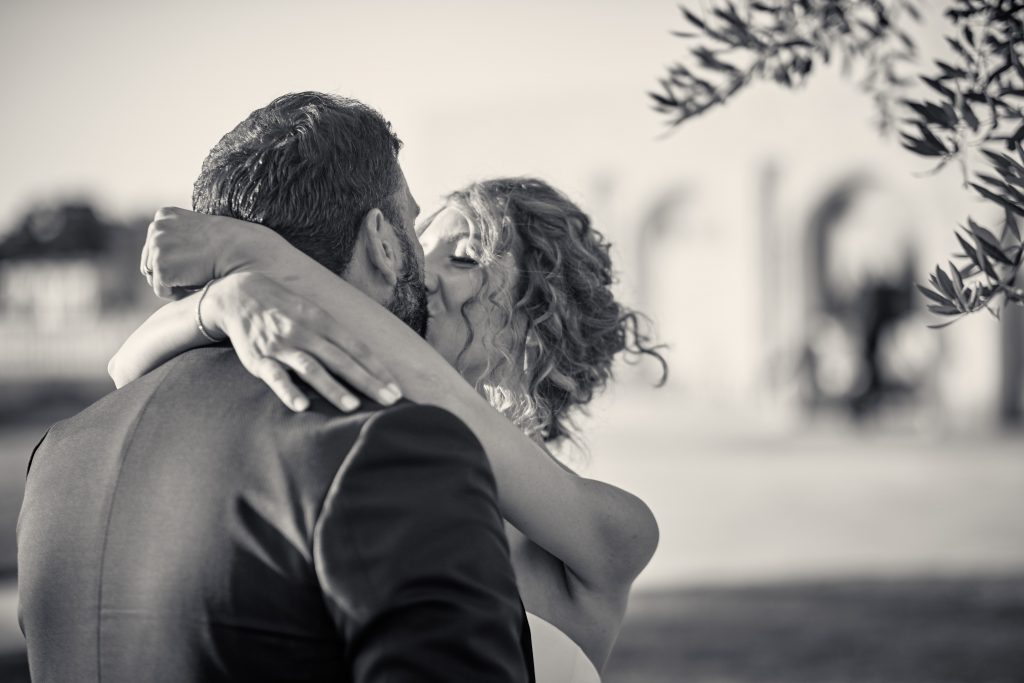 Black and white photo of couple embracing outdoors with woman's curly hair visible and palm fronds in background - © Pascal Recchia. All rights reserved.