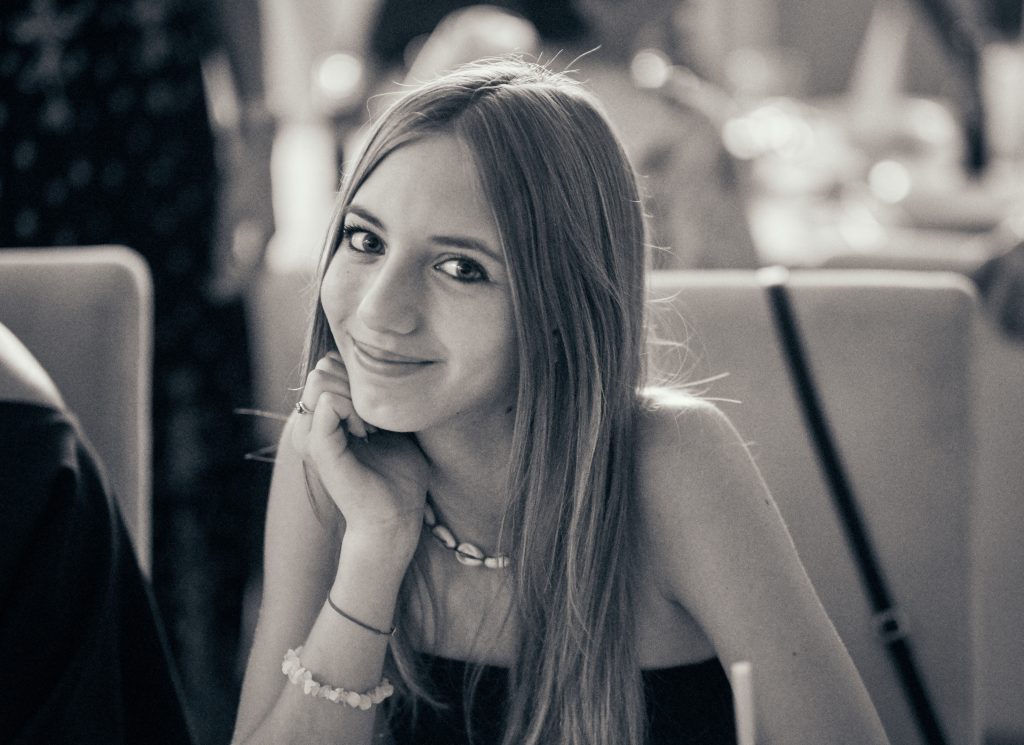 Woman with long hair and pearl bracelet sitting in restaurant, hand thoughtfully positioned near face - © Pascal Recchia. All rights reserved.