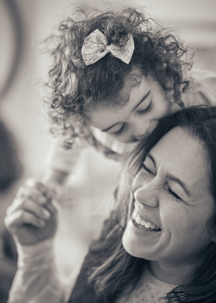 Black and white photo of a mother and her daughter laughing joyfully, one wearing a decorative hair bow - © Pascal Recchia. All rights reserved.