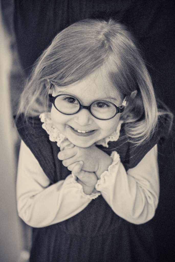 Young girl with glasses and blonde hair smiling warmly in black and white portrait photo - © Pascal Recchia. All rights reserved.