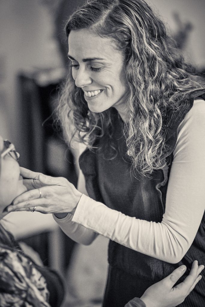 Black and white portrait of woman with curly hair smiling while embracing someone, conveying warmth and connection - © Pascal Recchia. All rights reserved.