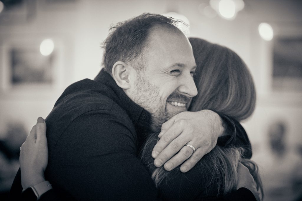 Middle-aged man with beard embracing woman in warm hug, smiling, black and white photo with soft bokeh background - © Pascal Recchia. All rights reserved.