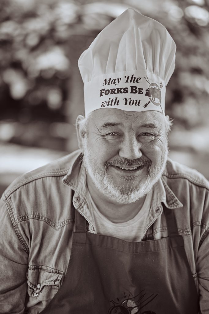 Smiling elderly man with white beard wearing chef's hat and apron that says "May The Forks Be With You" - © Pascal Recchia. All rights reserved.