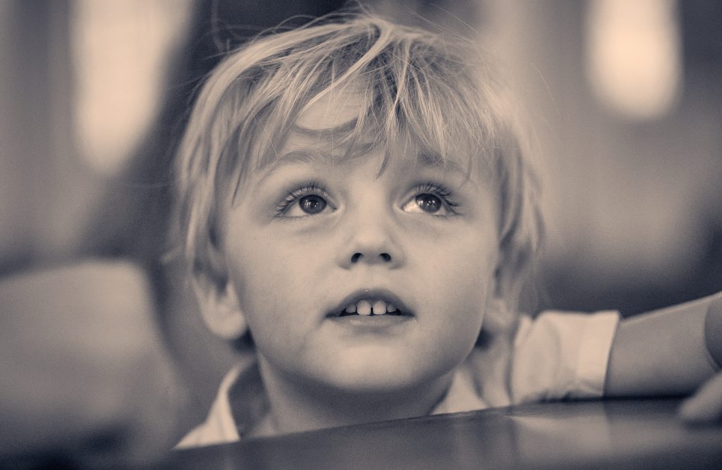 Close-up portrait of young child with tousled blonde hair and bright eyes looking up with wonder in sepia-toned photograph - © Pascal Recchia. All rights reserved.