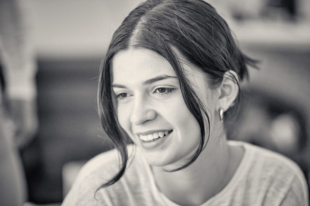 Young woman with dark hair smiling warmly in black and white portrait photo with soft lighting and blurred background - © Pascal Recchia. All rights reserved.