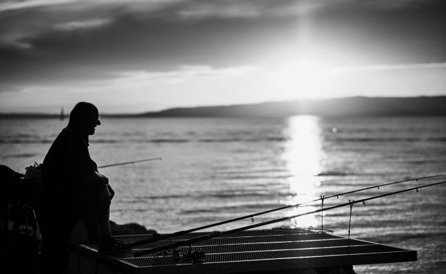 moments-oh-life-hungary-pascal-recchia-08072020 Silhouette of person fishing from dock at sunset with multiple fishing rods, water reflecting golden light - © Pascal Recchia. All rights reserved.